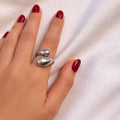 Anillo plateado KAVRA con diseño doble orgánico y acabado pulido, resistente al agua, sobre mano con uñas rojas en fondo blanco