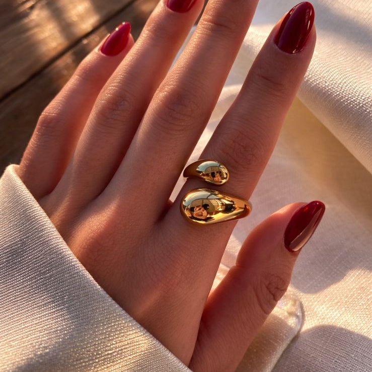 Anillo dorado ajustable KAVRA con diseño orgánico y acabado pulido, resistente al agua, sobre mano con uñas rojas en luz natural