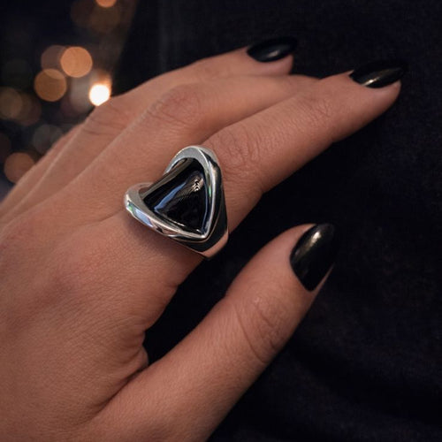 Anillo plateado KAVRA con piedra negra y diseño envolvente, resistente al agua, sobre mano con uñas negras en luz cálida nocturna