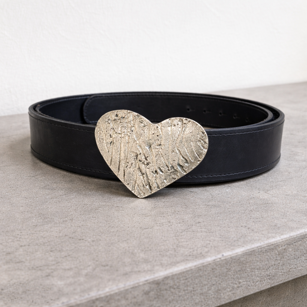 Cinturón negro de cuero con hebilla metálica en forma de corazón sobre superficie neutra